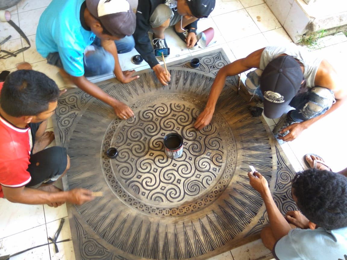 Craftsmen hand-carving a large round panel together